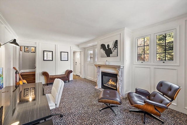 interior space featuring a healthy amount of sunlight, a decorative wall, crown molding, and a glass covered fireplace