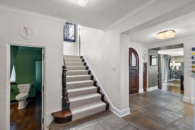 stairway with ornamental molding, a textured wall, a textured ceiling, and baseboards