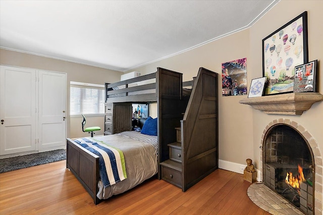 bedroom featuring baseboards, ornamental molding, a fireplace with flush hearth, and light wood-style floors