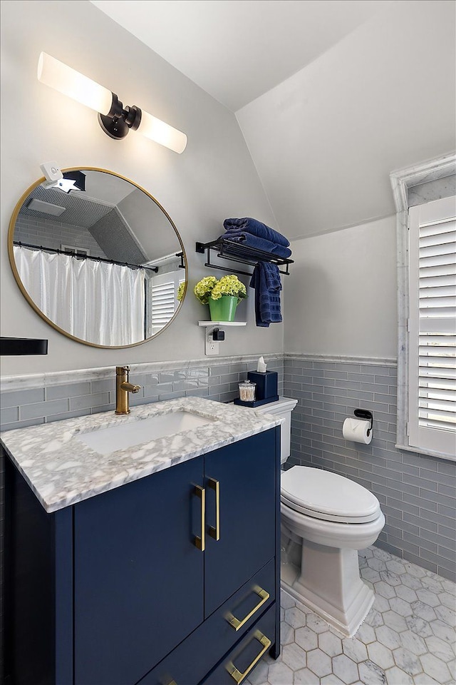 full bath featuring toilet, vanity, tile walls, vaulted ceiling, and tile patterned floors