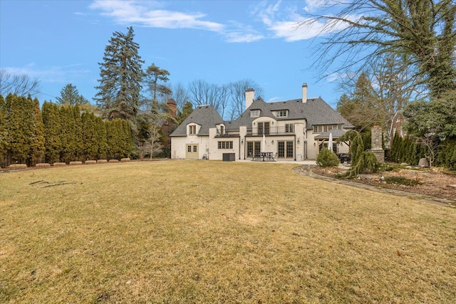 back of property featuring a patio area, a chimney, a lawn, and french doors