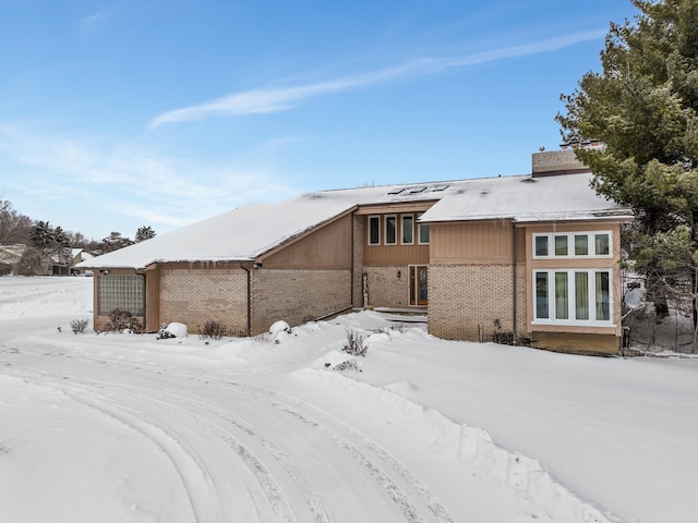 snow covered house featuring brick siding