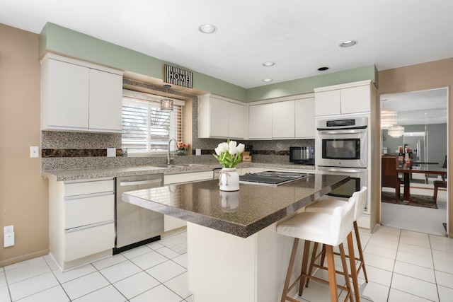 kitchen featuring stainless steel appliances, a sink, white cabinetry, tasteful backsplash, and a kitchen bar