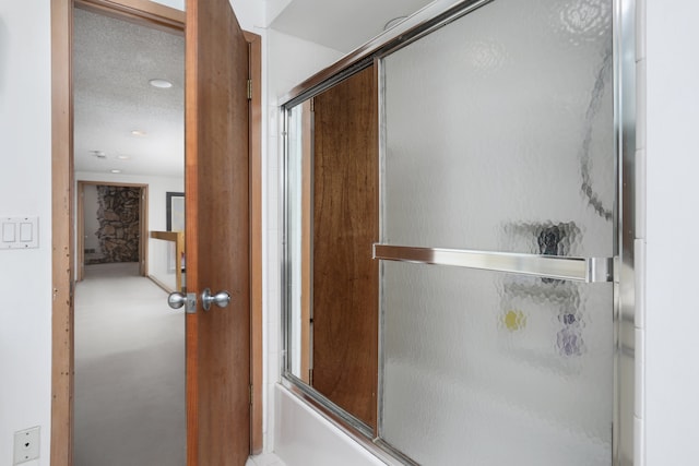 bathroom with a textured ceiling and bath / shower combo with glass door