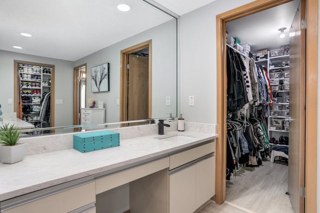 full bathroom with a walk in closet, vanity, recessed lighting, and wood finished floors