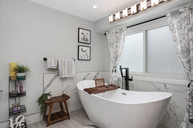 full bathroom with recessed lighting, a freestanding tub, wainscoting, and tile walls