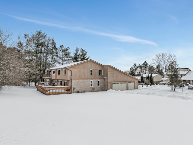 snow covered house with a garage and a wooden deck