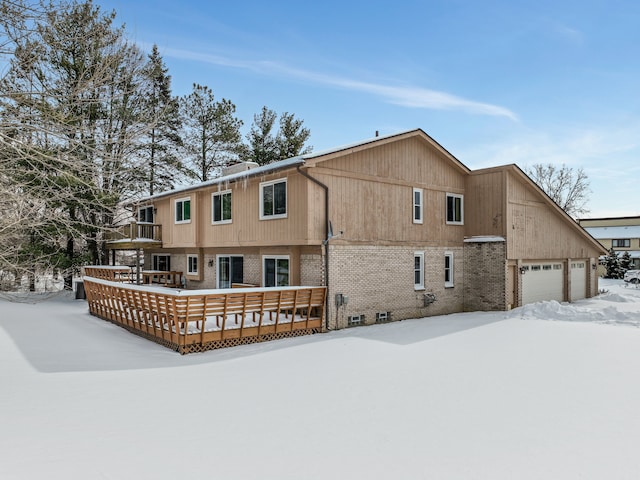 snow covered back of property featuring a deck and brick siding