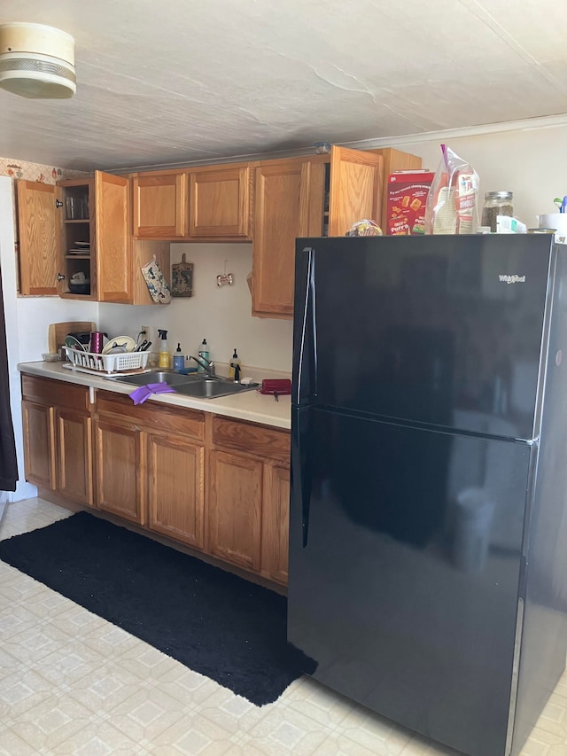 kitchen with open shelves, brown cabinetry, a sink, and freestanding refrigerator