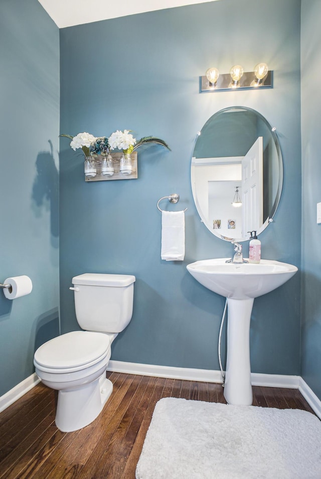 half bathroom with toilet, baseboards, and wood finished floors