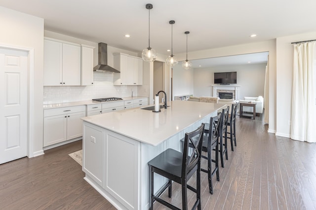 kitchen featuring dark wood finished floors, stainless steel gas stovetop, white cabinetry, a sink, and wall chimney range hood