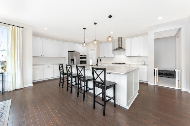 kitchen with a center island with sink, a breakfast bar area, stainless steel appliances, light countertops, and wall chimney range hood