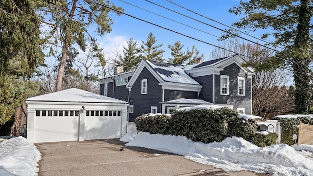 view of front of house with concrete driveway, an outdoor structure, a chimney, and an attached garage