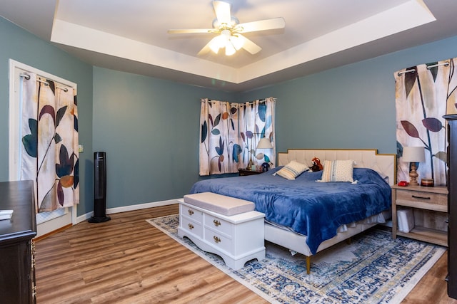 bedroom with a tray ceiling, ceiling fan, baseboards, and wood finished floors