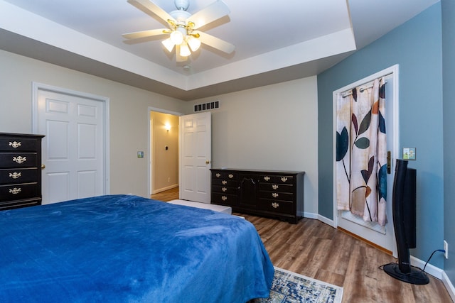 bedroom with a tray ceiling, wood finished floors, visible vents, and baseboards