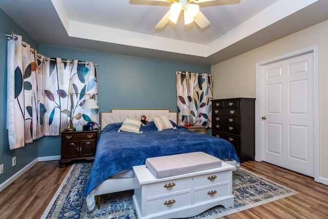 bedroom with a raised ceiling, ceiling fan, baseboards, and wood finished floors