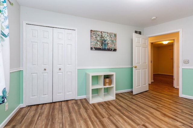 unfurnished bedroom with baseboards, a closet, visible vents, and wood finished floors