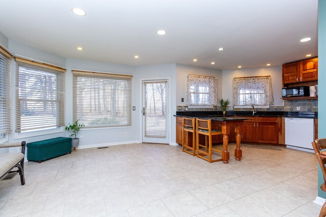 kitchen with white dishwasher, recessed lighting, a sink, baseboards, and dark countertops