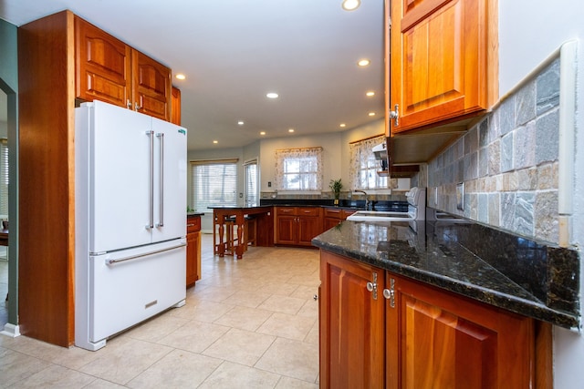 kitchen with a peninsula, high end fridge, brown cabinets, decorative backsplash, and dark stone counters