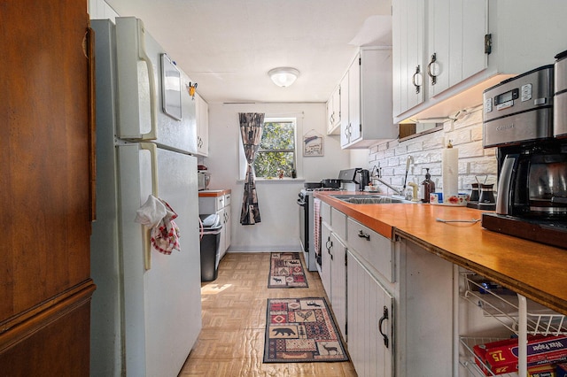 kitchen with stainless steel electric stove, backsplash, freestanding refrigerator, white cabinets, and a sink