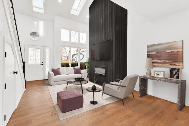 living room featuring a skylight, a fireplace, recessed lighting, a towering ceiling, and wood finished floors