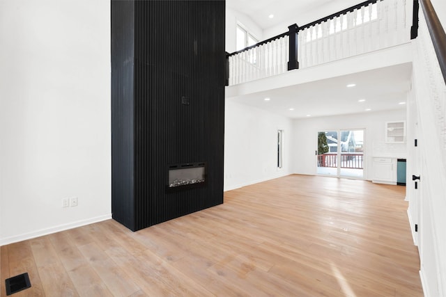 unfurnished living room featuring a large fireplace, a high ceiling, wood finished floors, visible vents, and baseboards