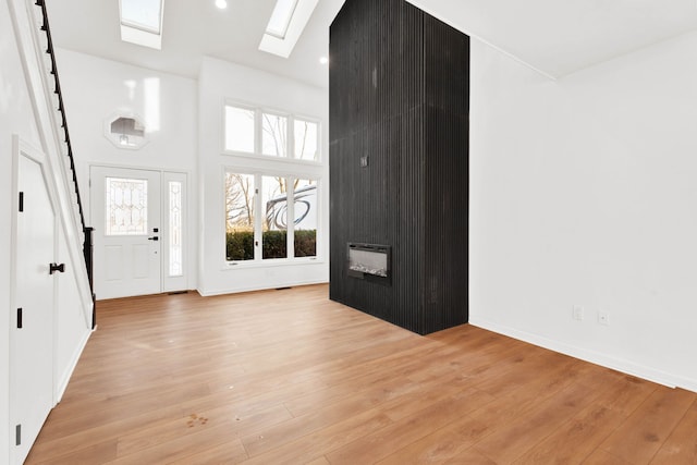 foyer entrance featuring a skylight, a large fireplace, a towering ceiling, light wood-style floors, and recessed lighting