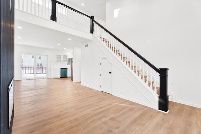 unfurnished living room featuring recessed lighting, visible vents, a towering ceiling, light wood-style floors, and stairs