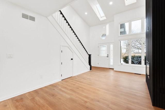 entryway with a skylight, a towering ceiling, visible vents, stairs, and light wood-style floors