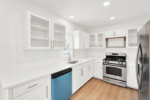 kitchen featuring stainless steel appliances, a sink, white cabinets, light wood-type flooring, and decorative backsplash