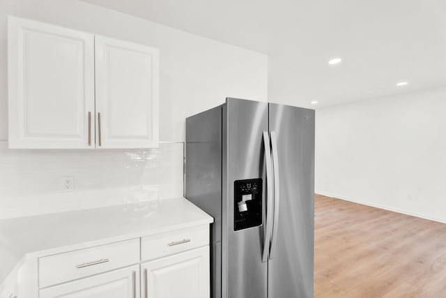 kitchen featuring white cabinets, light countertops, decorative backsplash, light wood finished floors, and stainless steel fridge