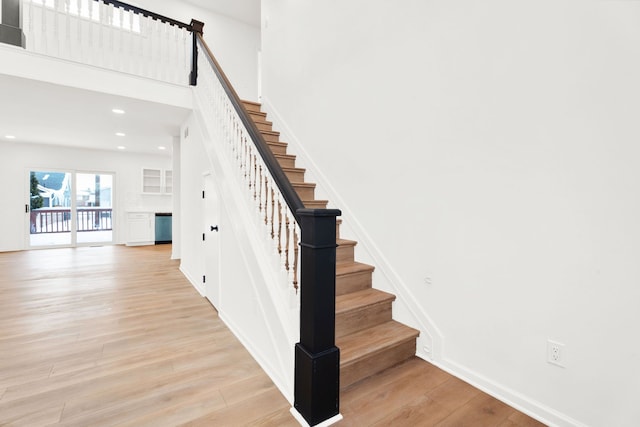 stairs featuring recessed lighting, a towering ceiling, baseboards, and wood finished floors