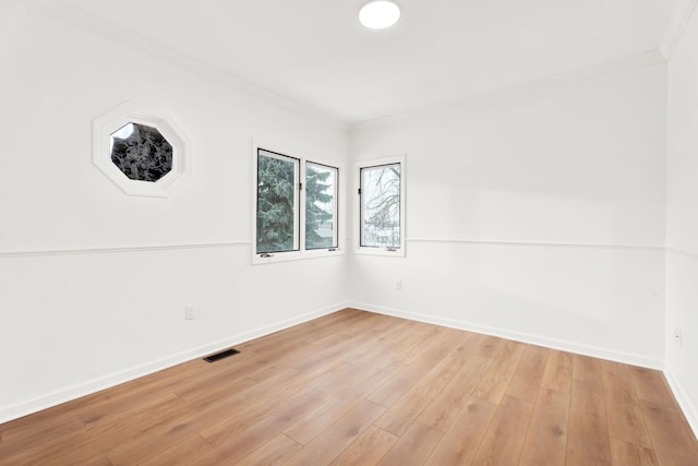 empty room featuring light wood-type flooring, visible vents, baseboards, and crown molding