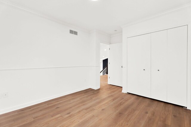 unfurnished bedroom with light wood-style flooring, visible vents, baseboards, ornamental molding, and a closet