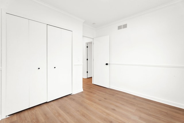 unfurnished bedroom with baseboards, visible vents, light wood-style flooring, crown molding, and a closet