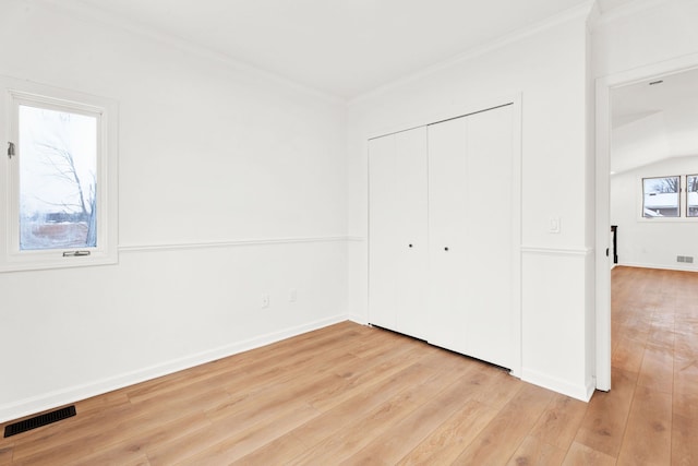 unfurnished bedroom with light wood finished floors, baseboards, visible vents, ornamental molding, and a closet