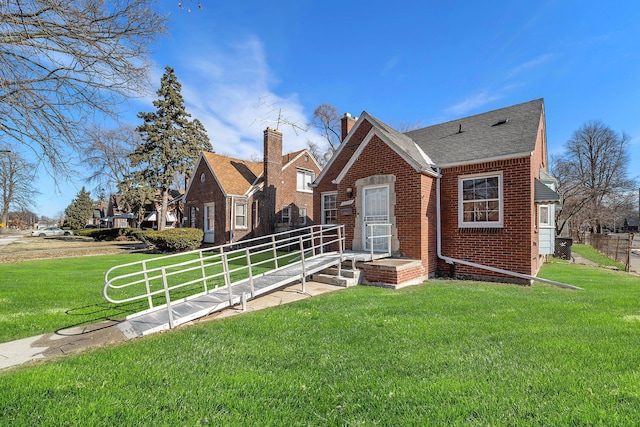 view of front facade with brick siding, a chimney, a front yard, and fence