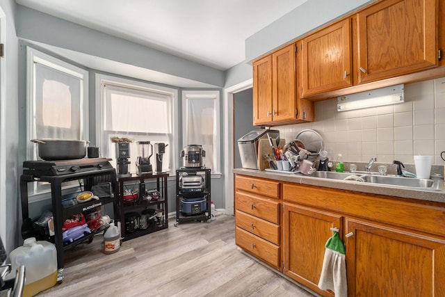 kitchen featuring brown cabinetry, a sink, decorative backsplash, light countertops, and light wood-type flooring