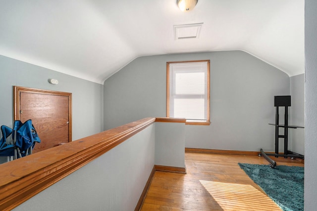 hallway with an upstairs landing, baseboards, light wood-style floors, and vaulted ceiling