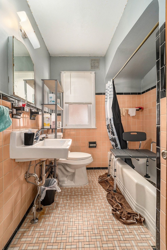 bathroom featuring tile walls, toilet, visible vents, and a wealth of natural light