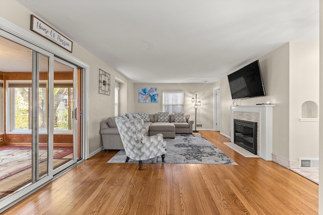 living room with a fireplace with flush hearth, baseboards, visible vents, and hardwood / wood-style floors