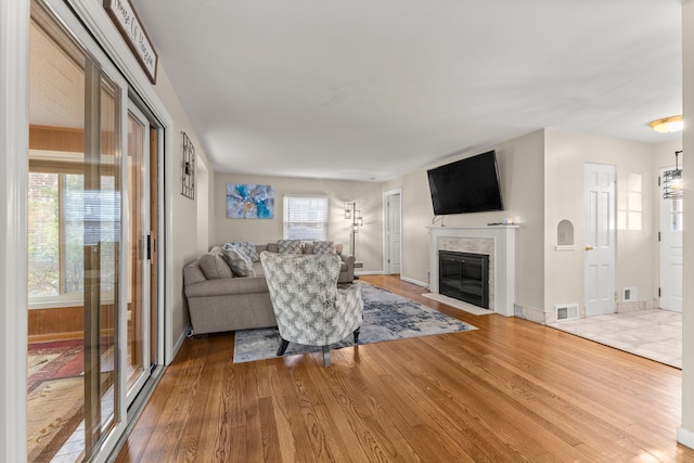 living area with a wealth of natural light, a fireplace, visible vents, and wood finished floors