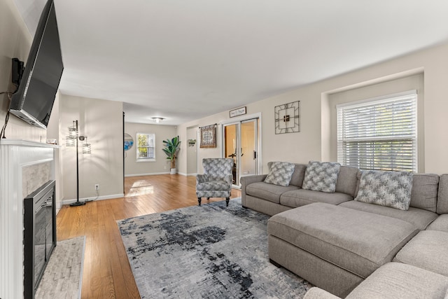 living room featuring light wood-style floors, a tile fireplace, and baseboards