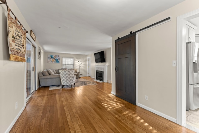 unfurnished living room featuring light wood-style floors, a barn door, baseboards, and a fireplace with flush hearth