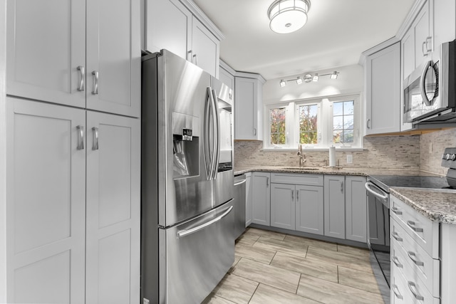 kitchen featuring decorative backsplash, appliances with stainless steel finishes, light stone countertops, gray cabinets, and a sink