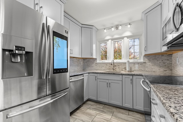 kitchen with appliances with stainless steel finishes, a sink, light stone countertops, and decorative backsplash