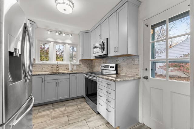 kitchen featuring tasteful backsplash, light stone counters, gray cabinets, stainless steel appliances, and a sink