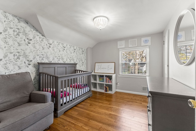 bedroom with visible vents, baseboards, vaulted ceiling, wood-type flooring, and wallpapered walls