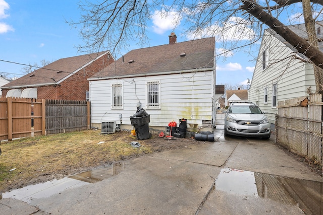 back of house featuring a shingled roof, a chimney, fence, and central air condition unit