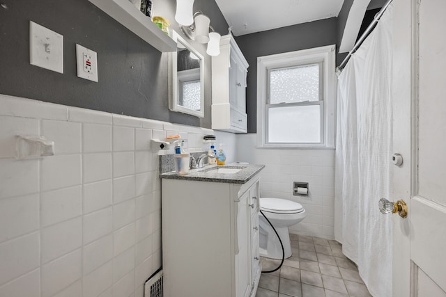 bathroom with a wainscoted wall, tile walls, toilet, vanity, and tile patterned floors